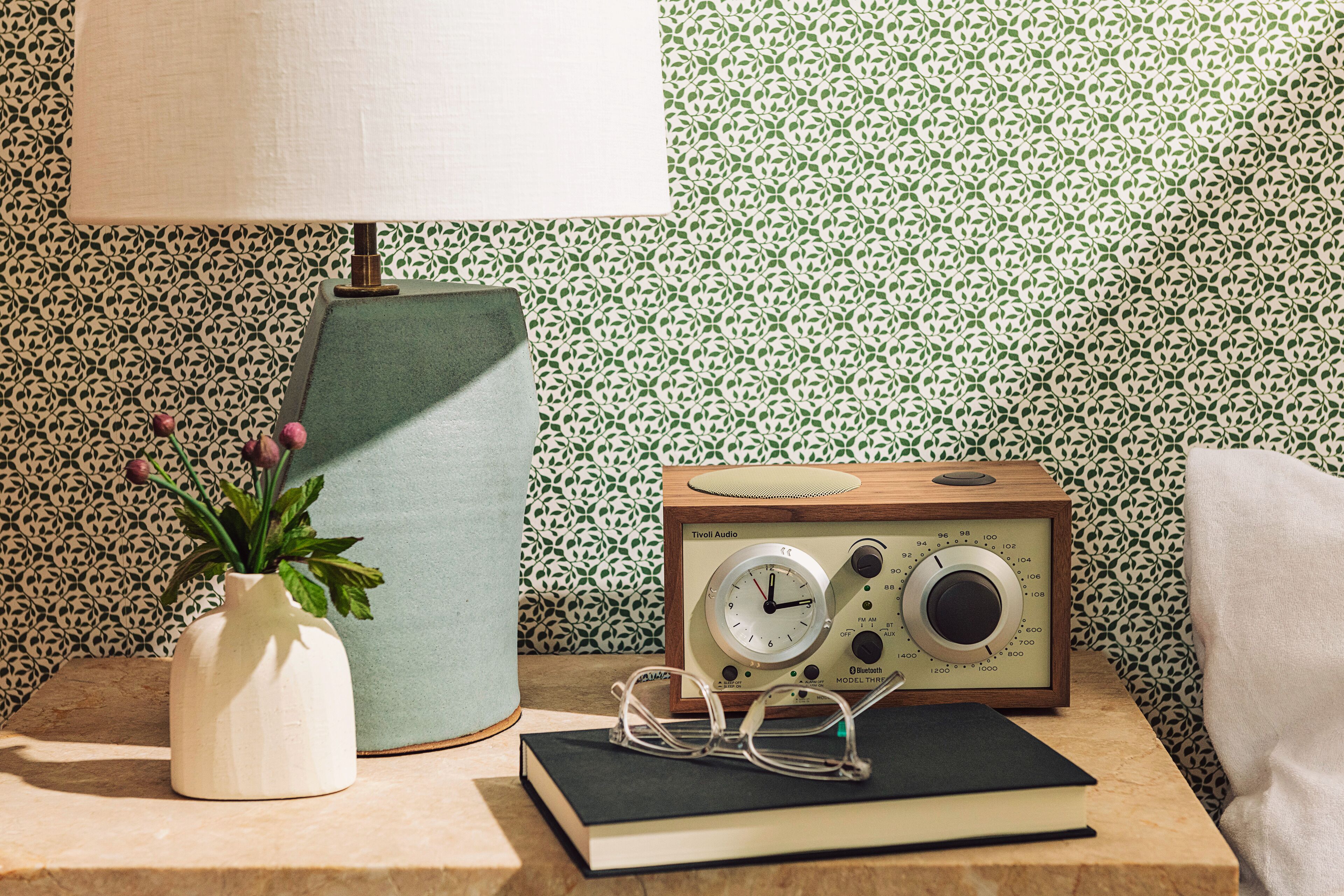 A vintage radio, a vase with a plant, a pair of glasses, and a book on a wooden surface.