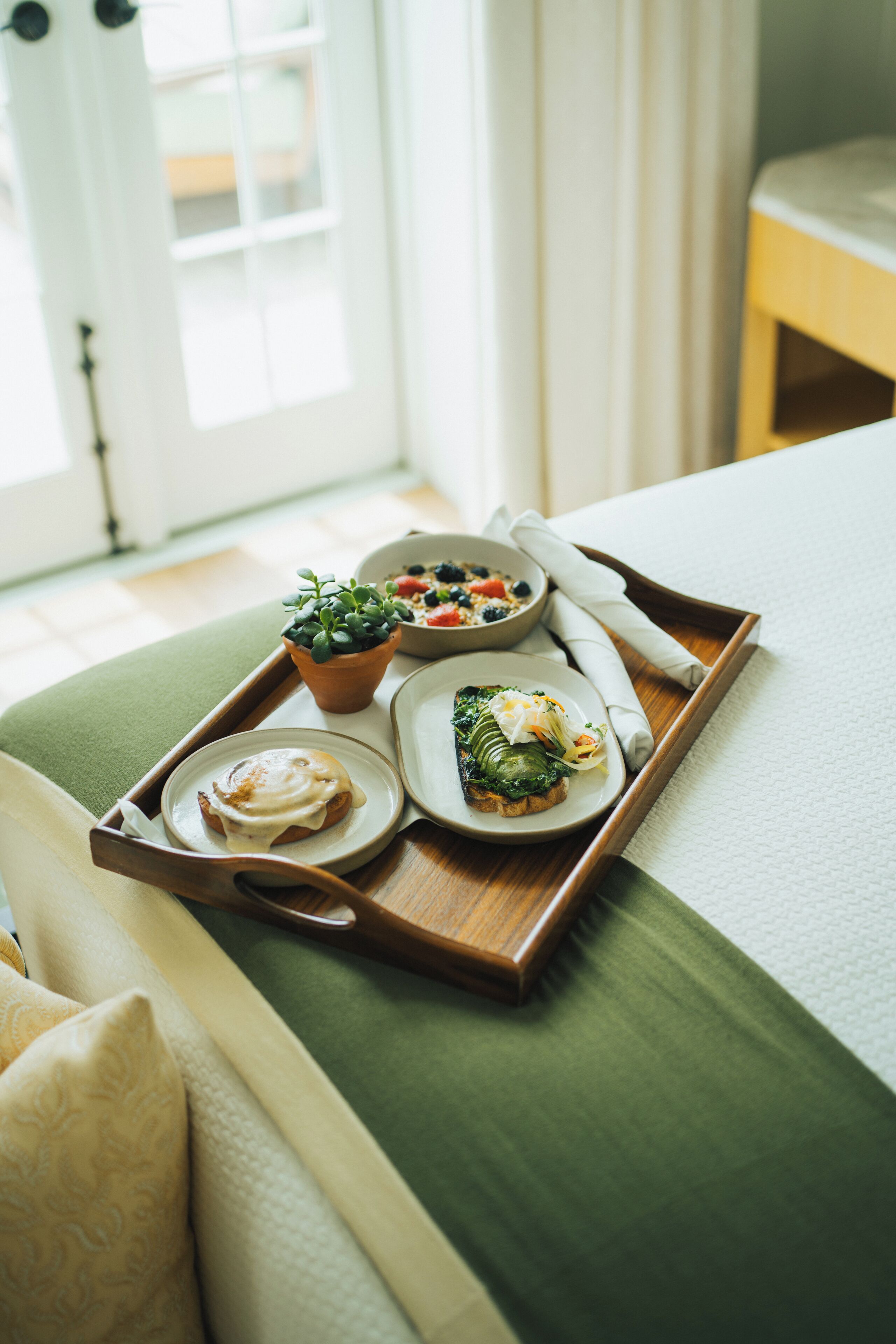 A tray with breakfast items including eggs, a salad, and a fruit bowl on a bed.