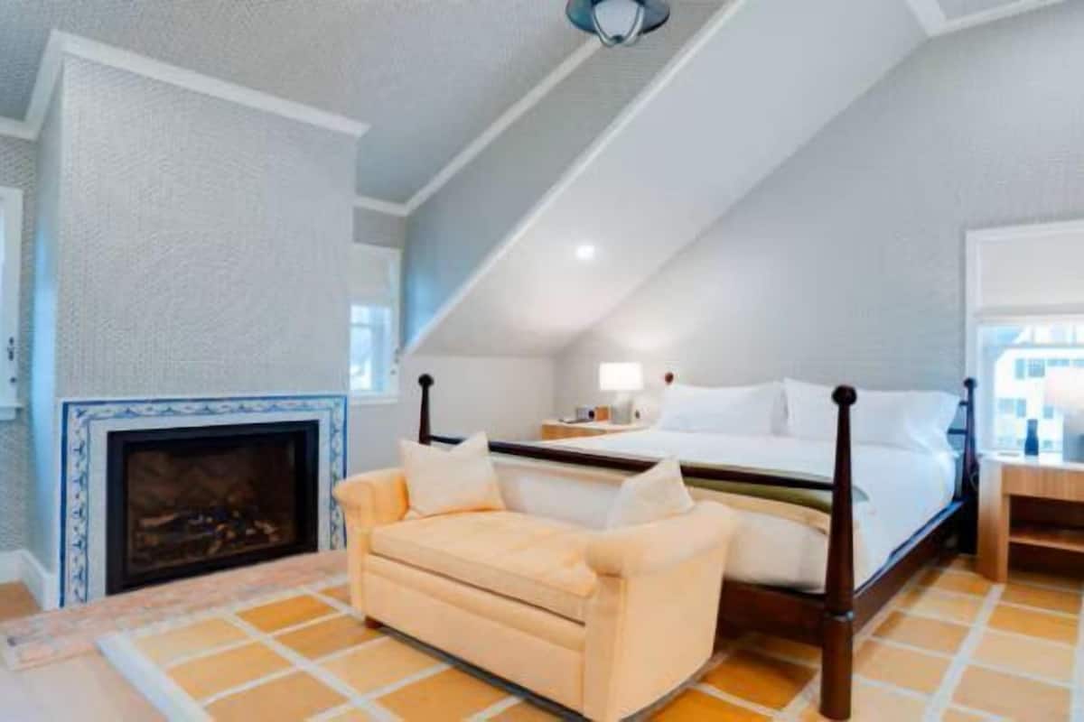 Une chambre à coucher comprenant un lit, une table de chevet, un canapé, une cheminée et une fenêtre donnant sur un beau paysage.