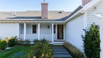 A white single-story house with a front porch, a brick chimney, and a small garden with a pathway leading to the door.