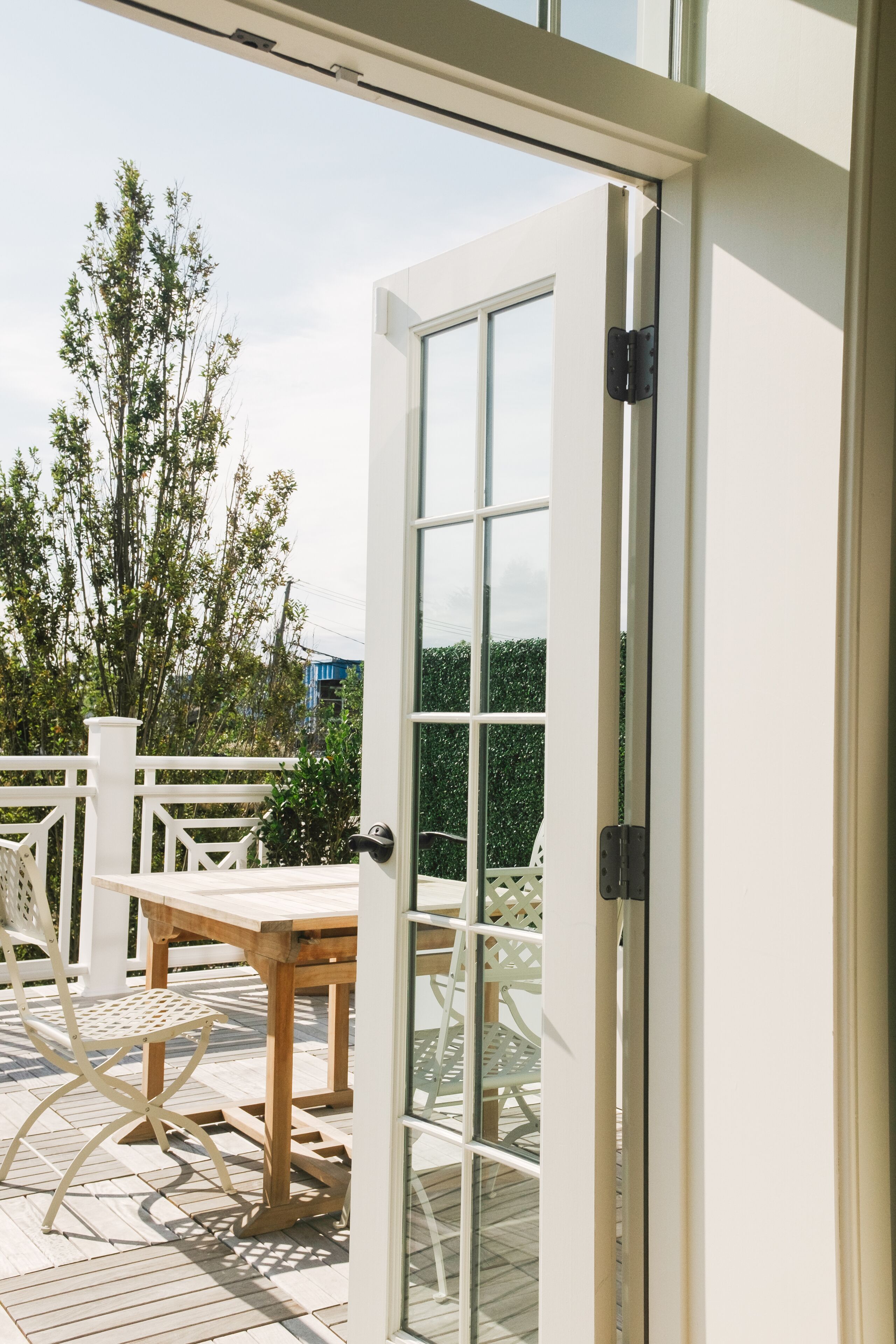 Una puerta de cristal abierta que da a un patio con una mesa y sillas de madera.