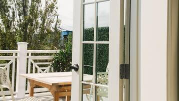 Una puerta de cristal abierta que da a un patio con una mesa y sillas de madera.
