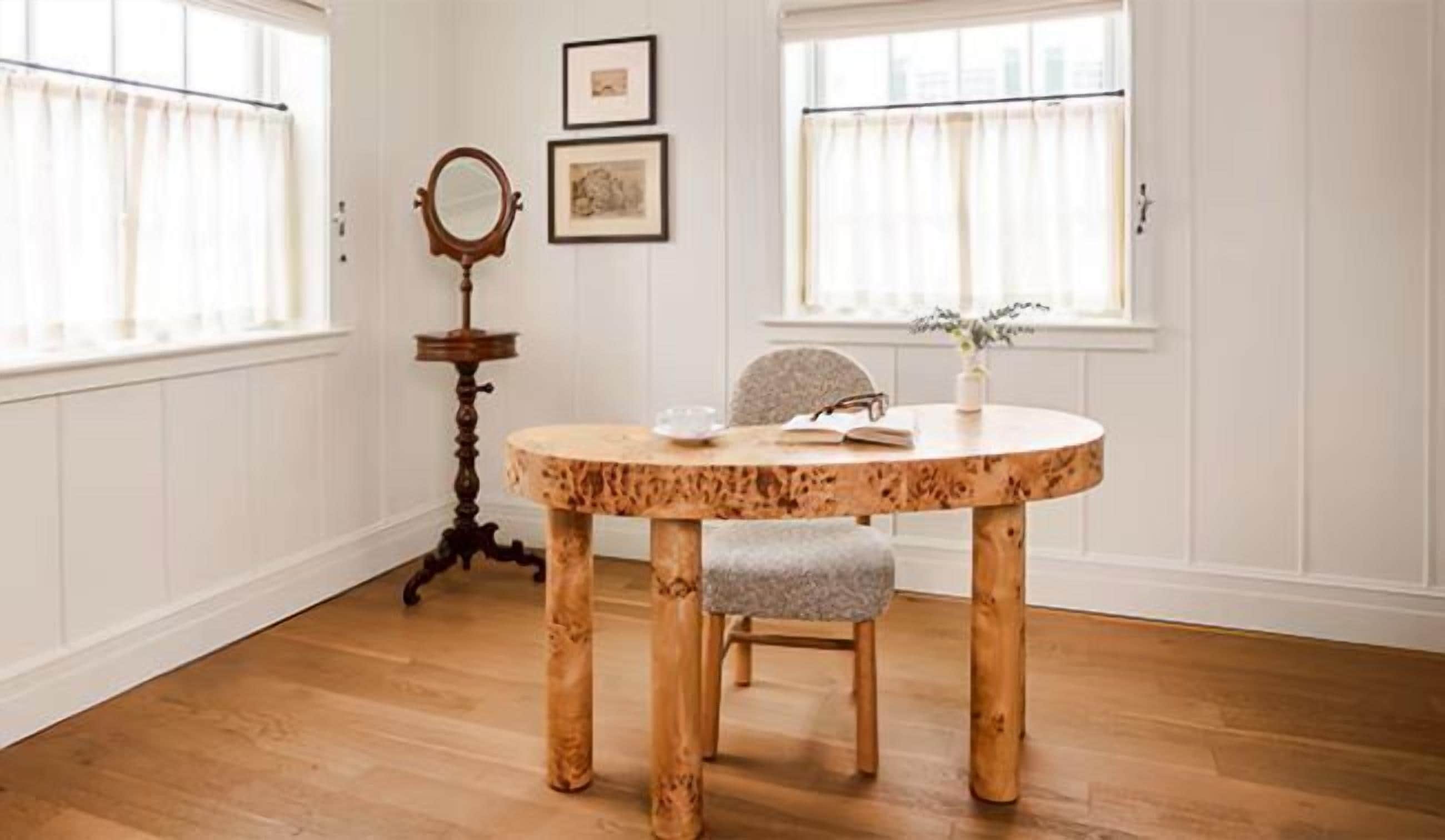 Una mesa de comedor redonda de madera, una silla, una mesita auxiliar con un espejo y dos cuadros en la pared.
