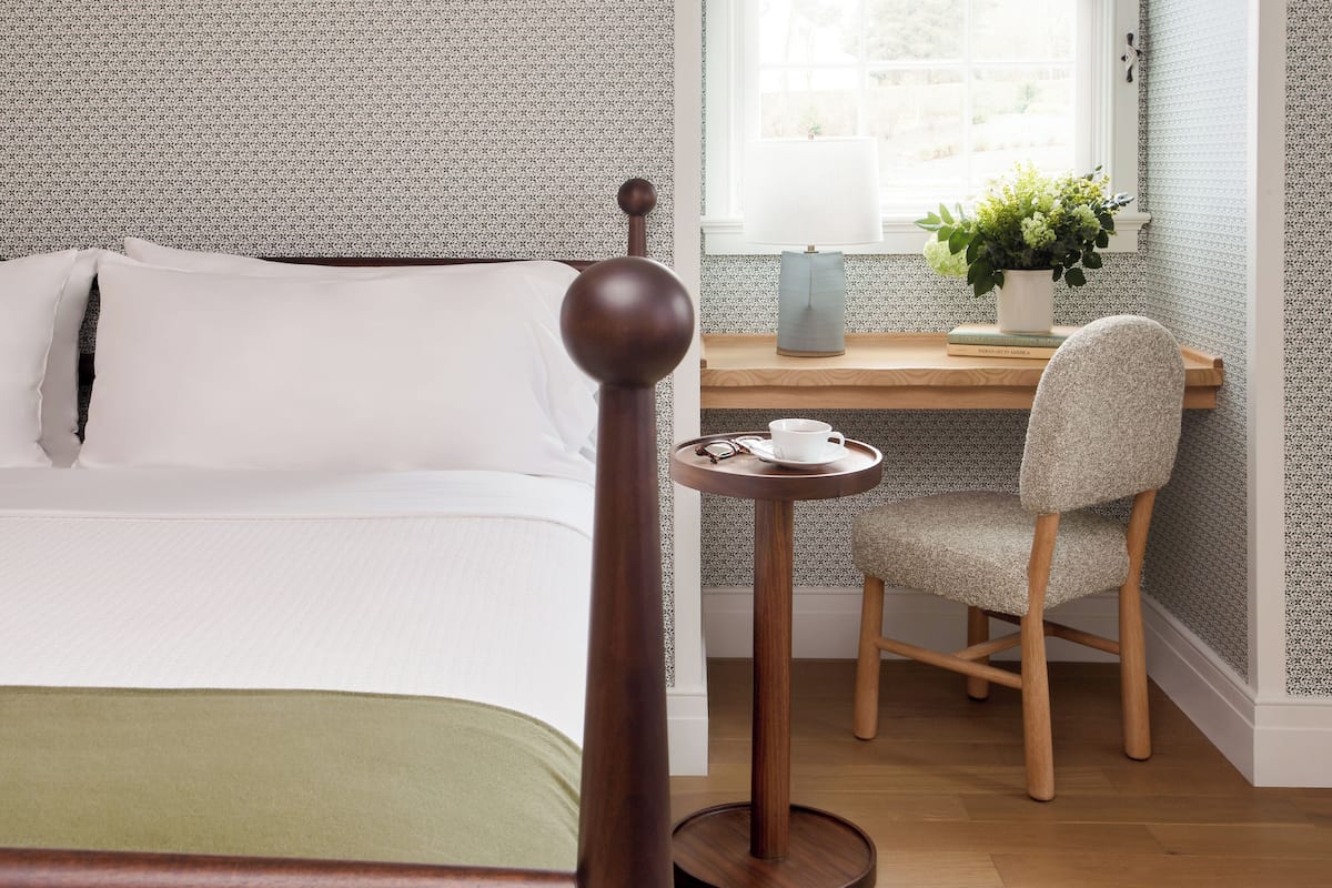 Une chambre à coucher bien rangée, avec un lit, une chaise, une petite table et une fenêtre donnant sur un beau paysage.