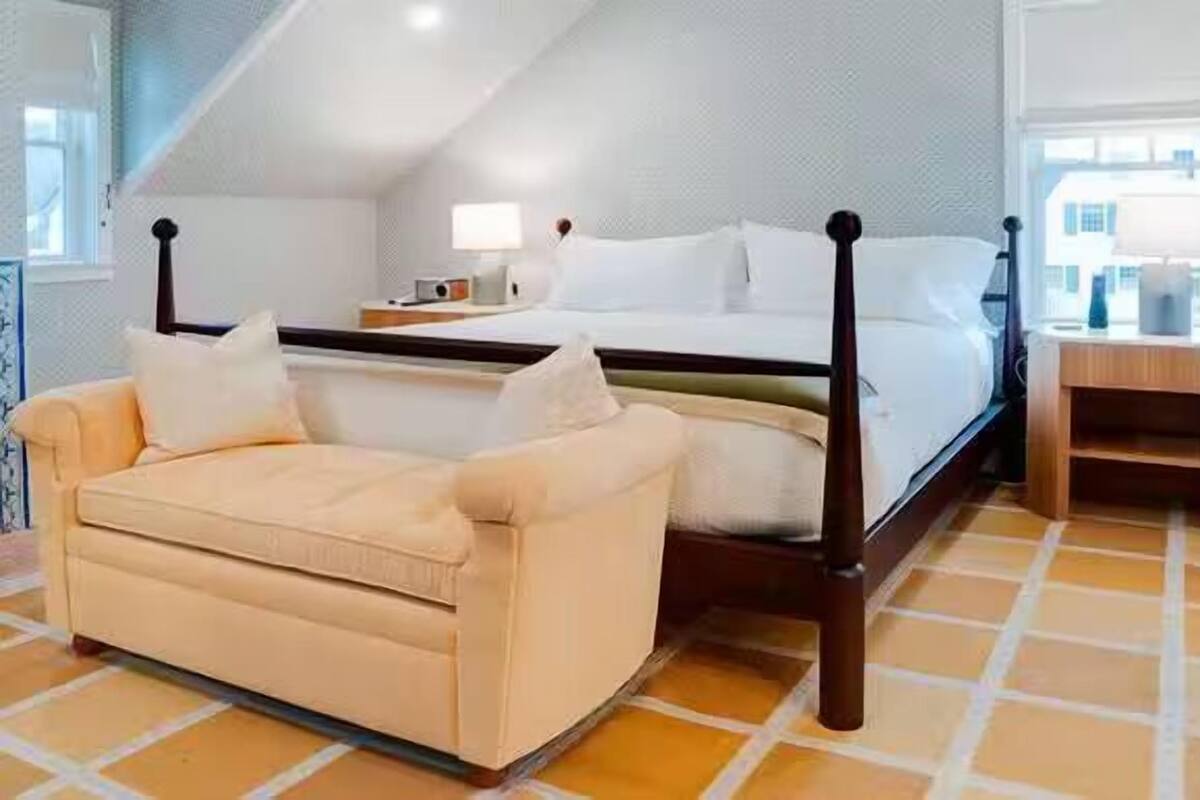 Une chambre à coucher comprenant un lit, une table de chevet, un canapé et une fenêtre donnant sur des immeubles.