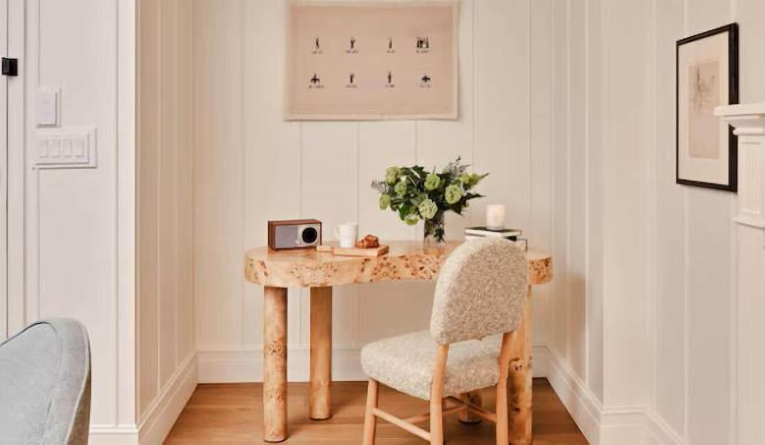 A room with a wooden table and chair, a radio, a vase with flowers, and a framed picture on the wall.