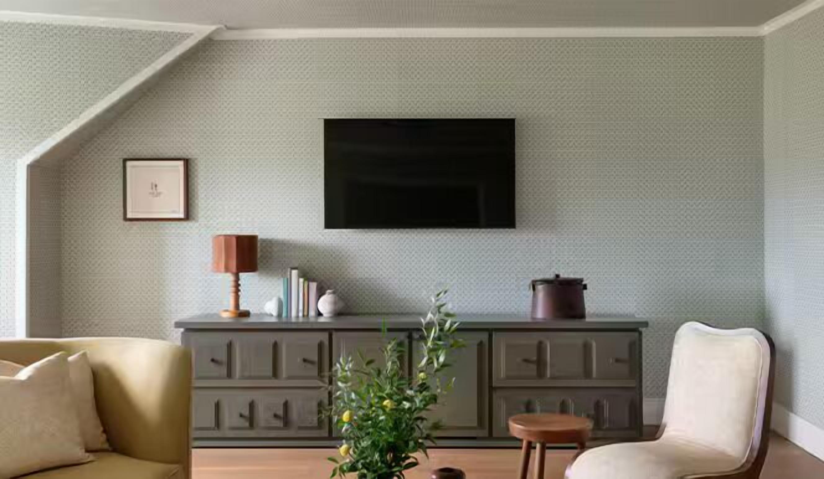 A living room with a sofa, a small table with a lamp, a cabinet with decorative items, and a television on the wall.