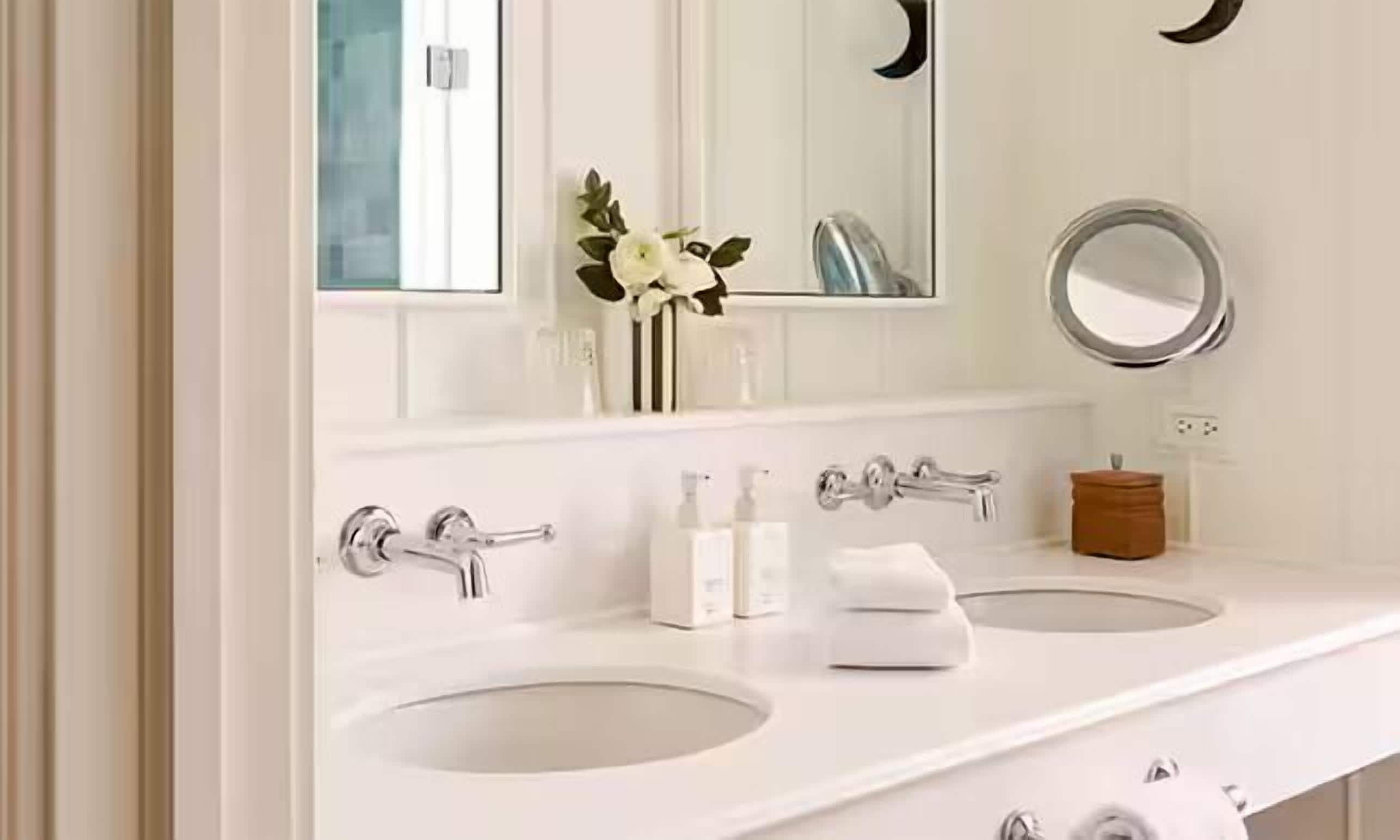 A bathroom with two sinks, a mirror, and a small vase with flowers.