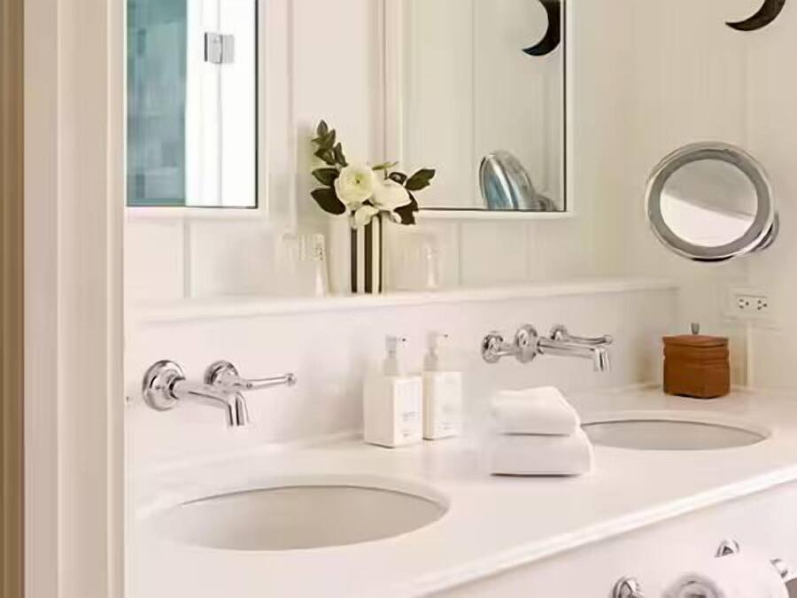 A bathroom with two sinks, a mirror, and a small vase with flowers.
