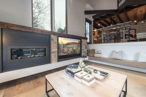 Una sala de estar moderna con chimenea, un televisor grande y una mesa de centro de madera con libros y objetos decorativos.