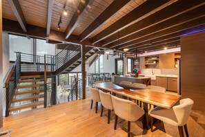 Una cocina moderna con armarios de madera, un comedor con mesa y sillas de madera, y una escalera que conduce a un nivel superior.