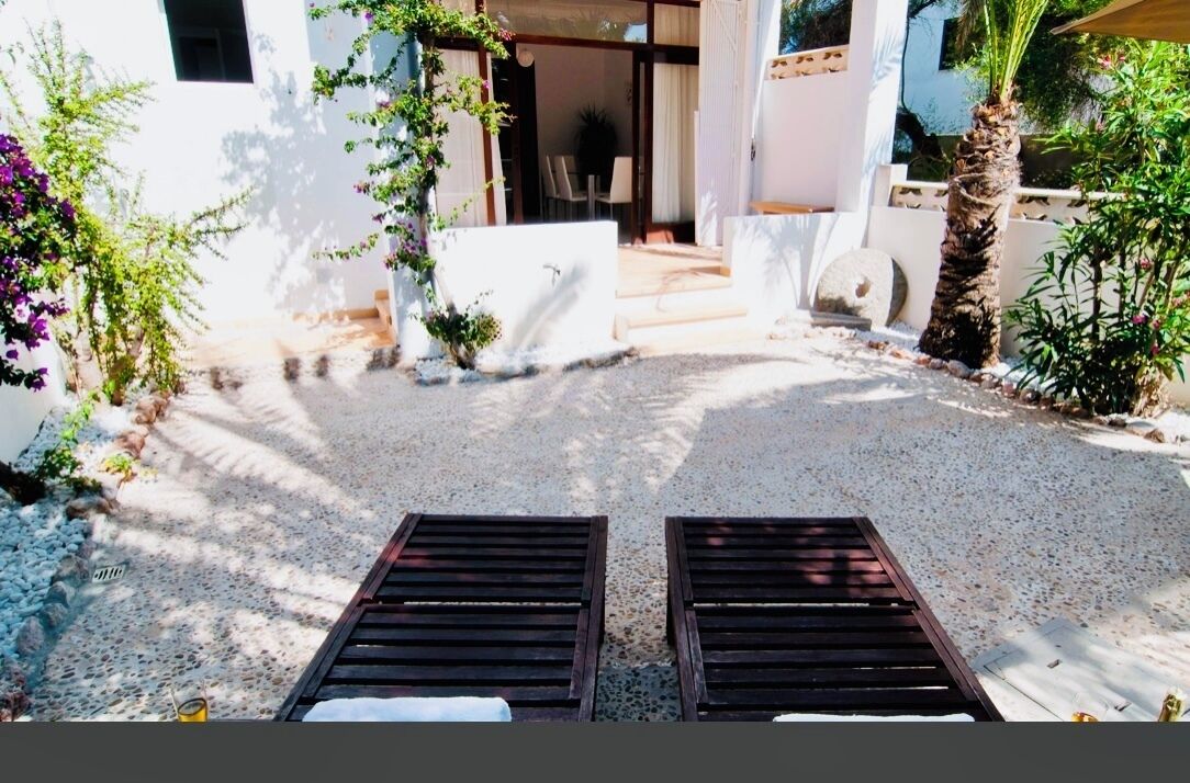 A courtyard with two wooden lounge chairs, a gravel path, and a building entrance.