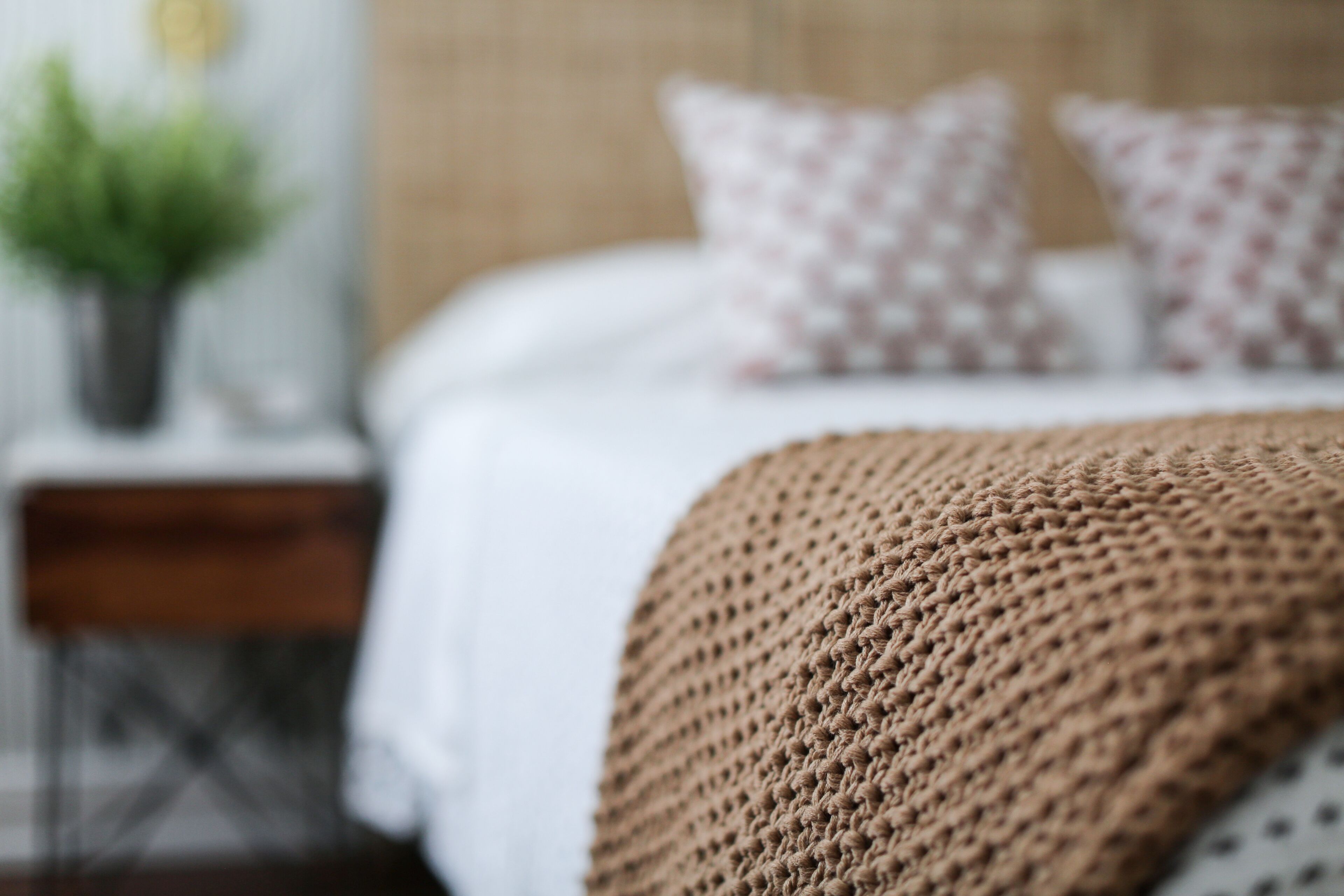 A bed with a knitted blanket and patterned pillows.