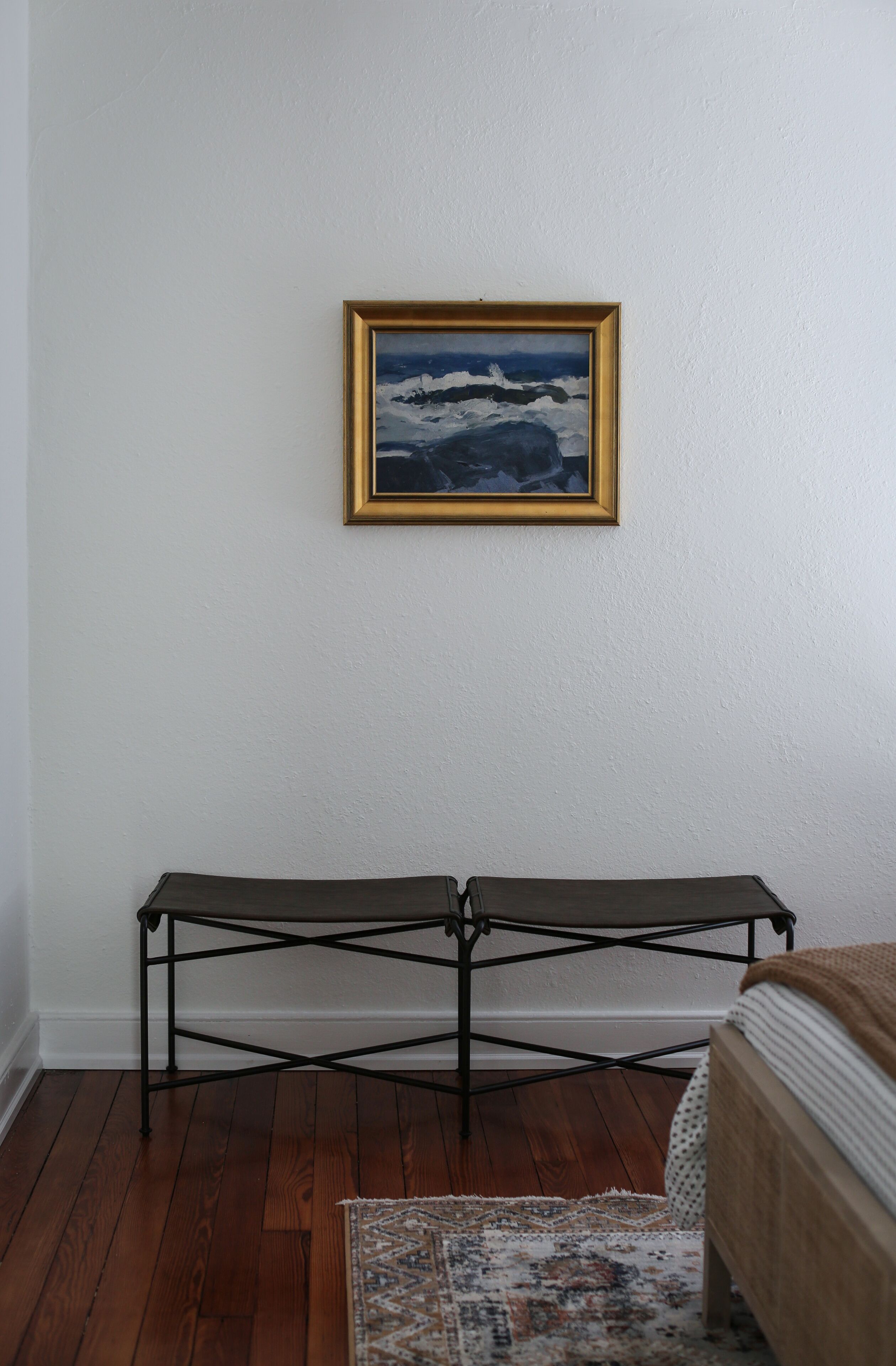 A room with a bed, a small table, and a framed painting on the wall.