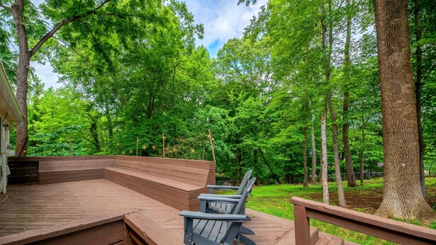 Une terrasse en bois, dotée de chaises Adirondack, et offrant une vue sur une zone boisée.