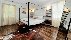 Un lit à baldaquin avec un couvre-lit et des oreillers blancs, un plancher en bois, un banc en cuir et un grand miroir.