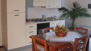 Une cuisine de taille réduite avec des meubles blancs, une cuisinière à gaz et un évier. Une table à manger, entourée de chaises, est agrémentée d’un centre de table floral.