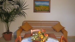 Une pièce comprenant un canapé, une table à manger agrémentée d’un arrangement floral, une plante en pot et un tableau encadré accroché au mur.