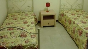 Une chambre à coucher avec deux lits, chacun agrémenté d’une literie à motifs floraux, une table de chevet avec une lampe et un tableau encadré au mur.