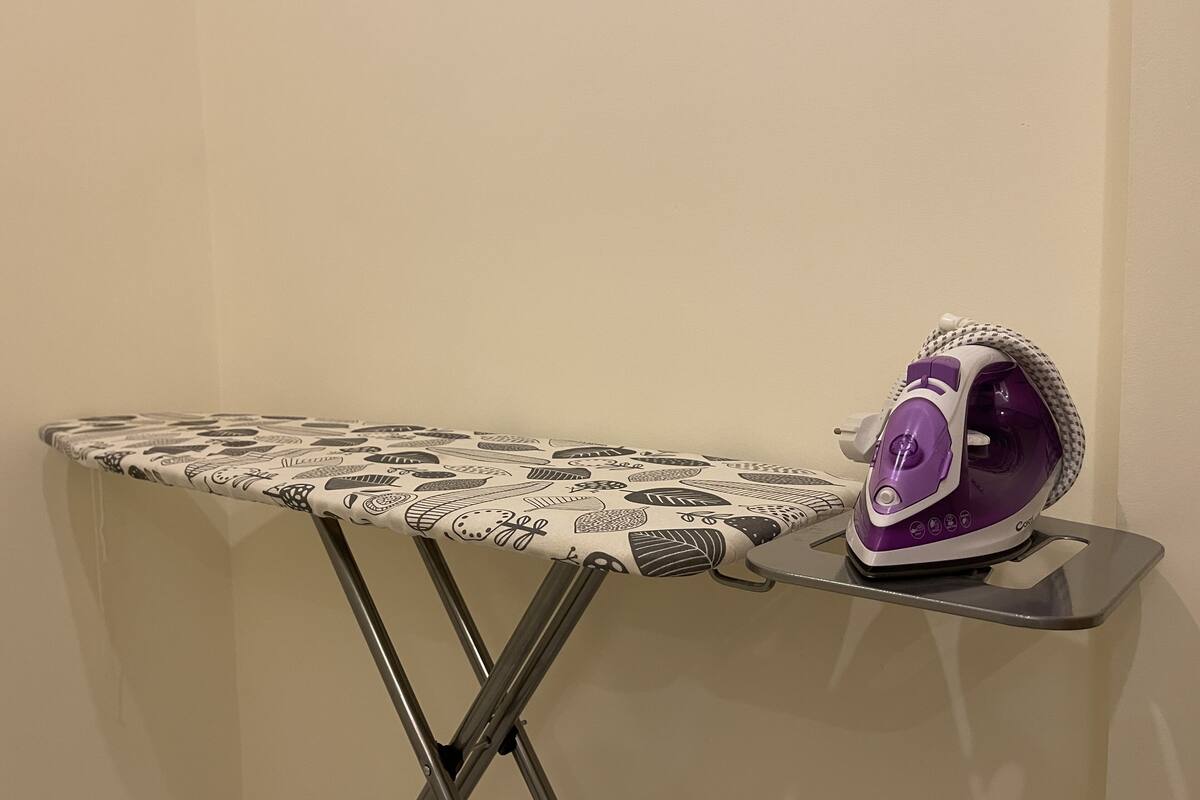 An ironing board with a patterned cloth and a purple iron on a stand.