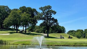 Golfkenttä, jossa on lampi, puita ja kirkas taivas.