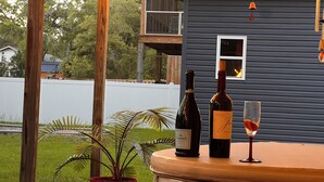 A patio area with a wooden table, a potted plant, and two bottles of wine on a round table. - Walk to Beach • Hot Tub • Pool Table • Ideal for Long Stays (Oak Island)