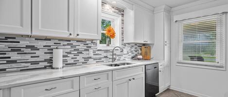 A modern kitchen with white cabinetry, a tiled backsplash, and a window with blinds.