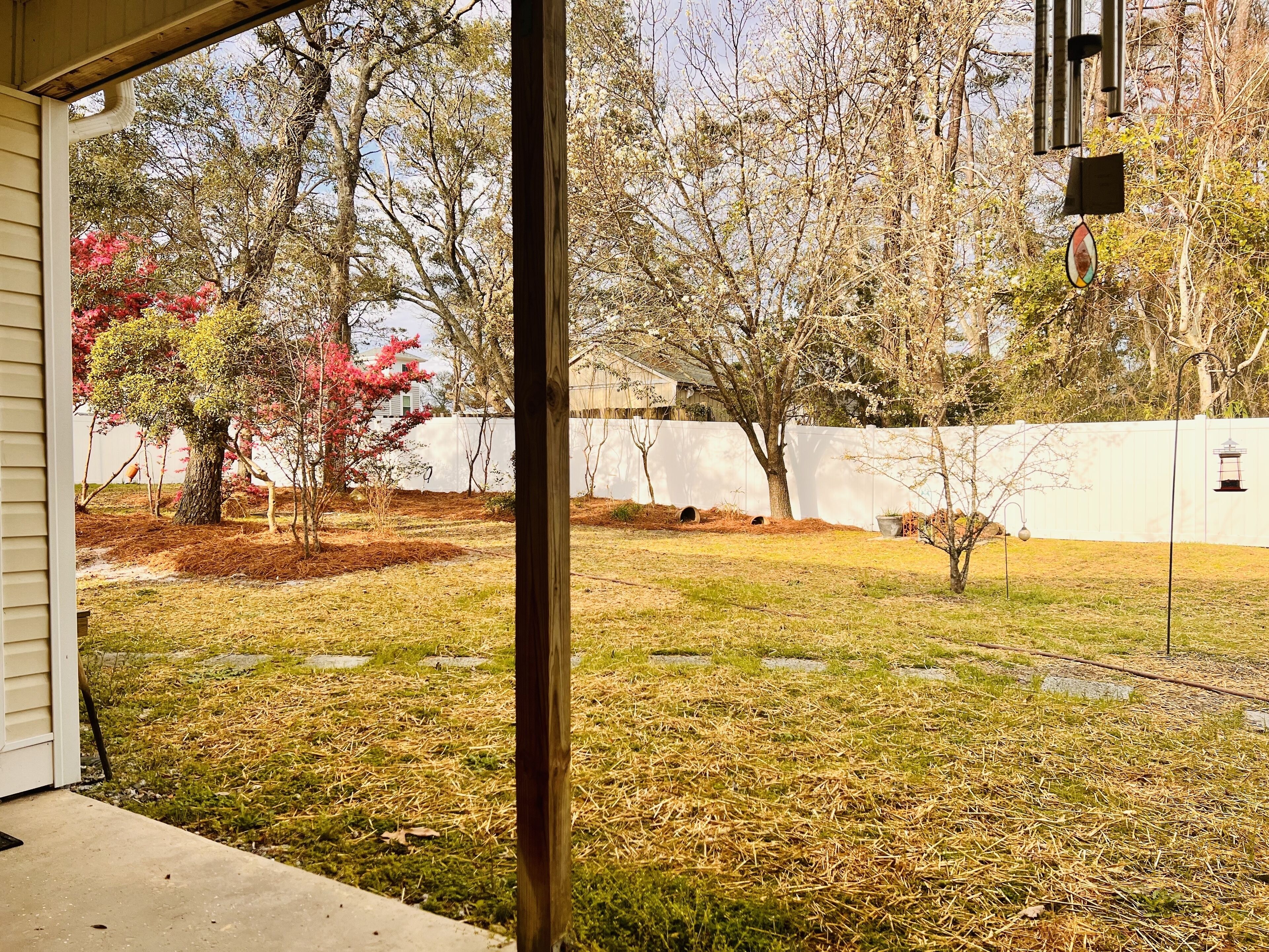 A backyard with a white fence, trees, and a wooden post.