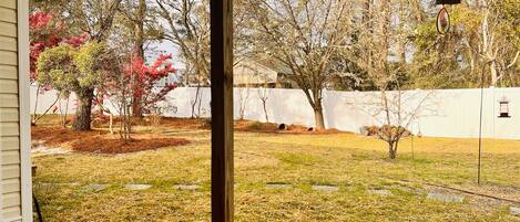 A backyard with a white fence, trees, and a wooden post.