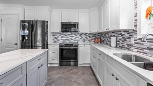 A modern kitchen with white cabinetry, stainless steel appliances, and a tiled backsplash. - Walk to Beach • Hot Tub • Pool Table • Ideal for Long Stays (Oak Island)