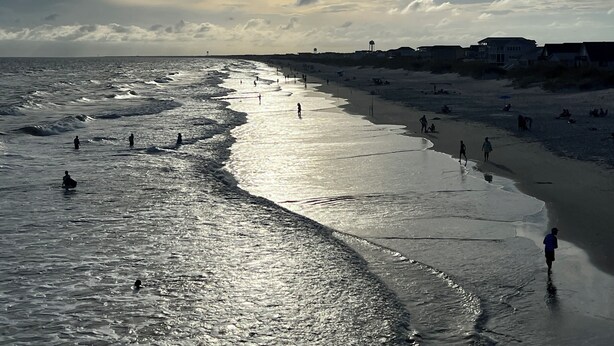 A beach with waves, people, and buildings in the background. - Walk to Beach • Hot Tub • Pool Table • Ideal for Long Stays (Oak Island)