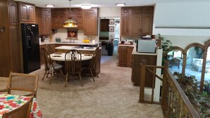 A kitchen with wooden cabinets, a dining table with chairs, a refrigerator, and a hanging light fixture. - Nestled near woods and creek, this large home is near state parks and colleges.. (Hillsboro)