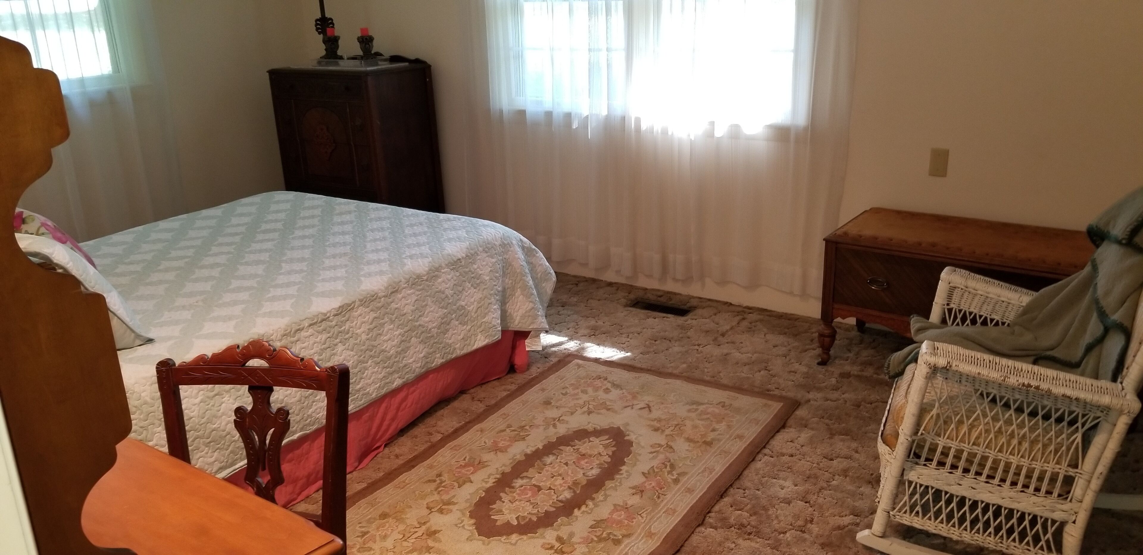 A bedroom with a bed, a wooden dresser, a chair, and a window with curtains.
