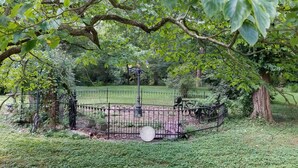 A fenced outdoor area with a bench and a statue, surrounded by trees and greenery. - Nestled near woods and creek, this large home is near state parks and colleges.. (Hillsboro)