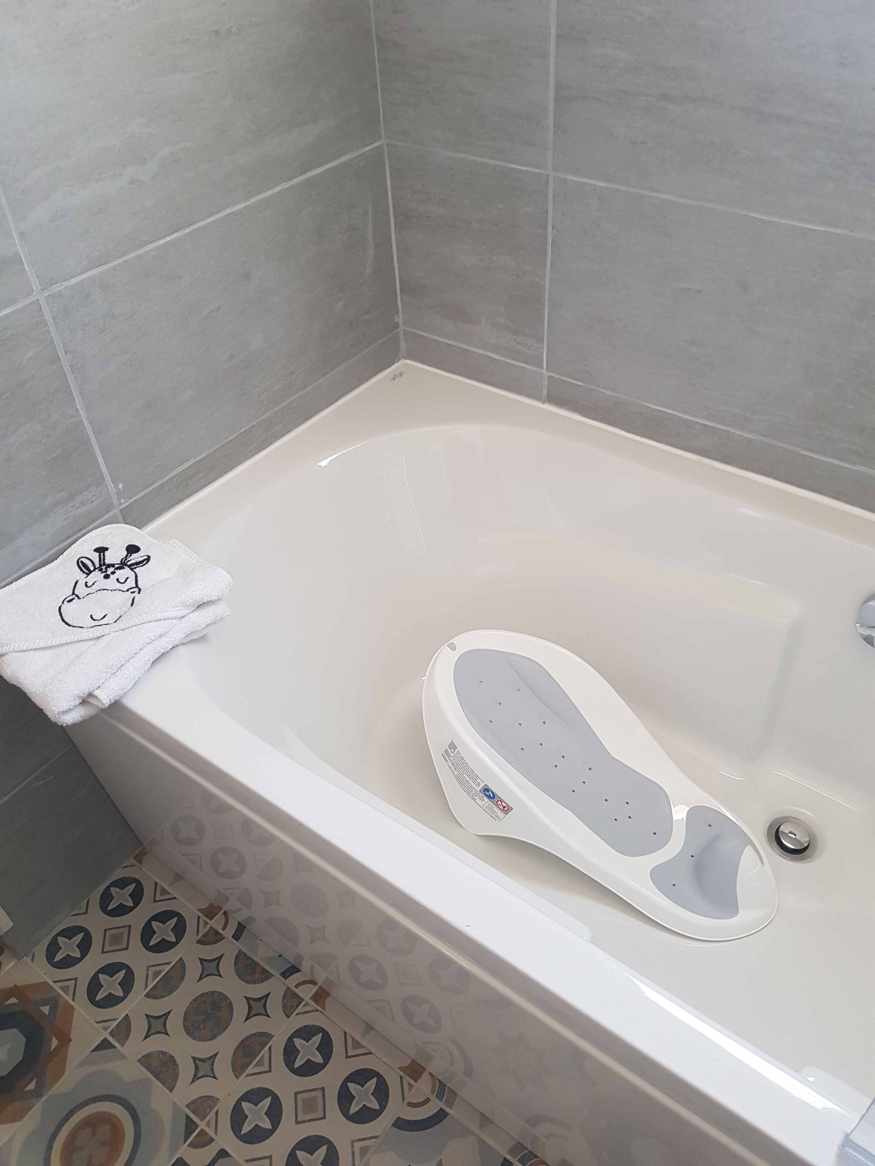 A bathtub with a white towel and slippers, tiled walls, and patterned floor tiles.