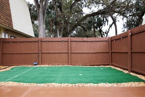 Un patio trasero cercado con césped artificial y un patio de concreto.