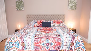Una cama con una colcha de diseño colorido, dos lámparas de noche y un cabecero capitonado.