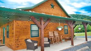 A log cabin with a green roof, wooden exterior, and a porch with wicker furniture and hanging flower baskets. - Luxury cabin with mountain views (Flintstone)