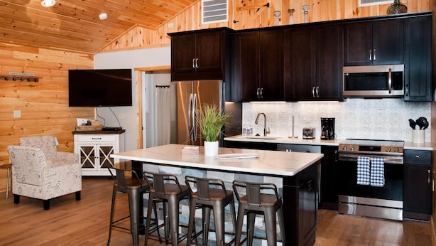 A modern kitchen with wooden walls, stainless steel appliances, and a bar area with stools. - Luxury cabin with mountain views (Flintstone)