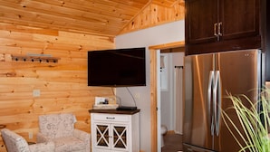 A wooden-paneled room with a flat-screen TV, a white cabinet with drawers, a patterned armchair, and a stainless steel refrigerator. - Luxury cabin with mountain views (Flintstone)