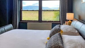 A hotel room with a large bed, a window with a view of a field and mountains, a bedside lamp, and a headboard. - 4 bedroom accommodation in Appin (Appin)
