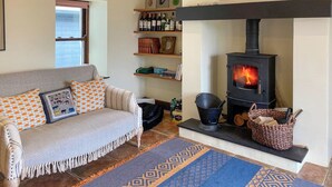 A cozy living room with a sofa, fireplace, and shelves with books and bottles. - 4 bedroom accommodation in Appin (Appin)