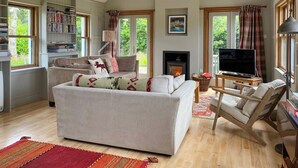 A spacious living room with a fireplace, a television, and a bookshelf. - 4 bedroom accommodation in Appin (Appin)