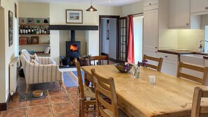 A cozy living room with a fireplace, a dining table, and a kitchen area. - 4 bedroom accommodation in Appin (Appin)