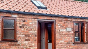 A brick building with a tiled roof, a wooden door, and two flower planters. - 1 bedroom accommodation in Addlethorpe, near Skegness (Addlethorpe, near Skegness)