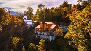 Une cabane en bois dotée d’un balcon, entourée d’une forêt dense et avec une montagne en arrière-plan.