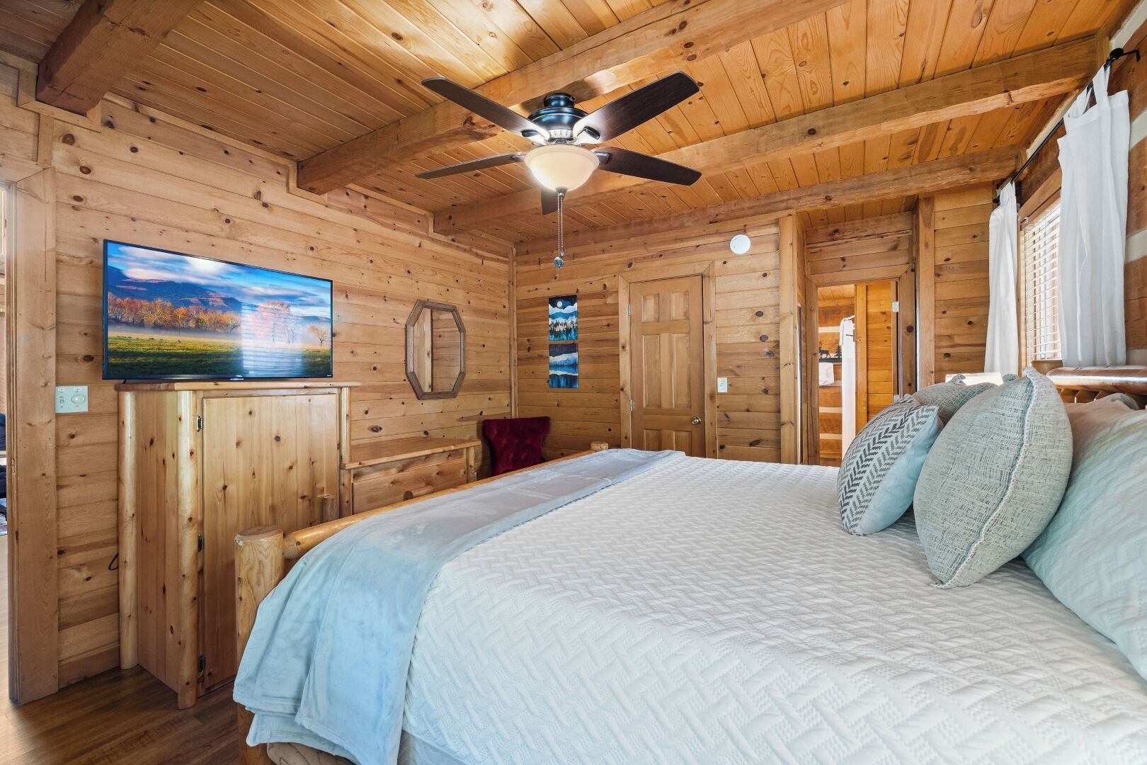 Een slaapkamer in een houten hut, met een bed, plafondventilator en een schilderij aan de muur.