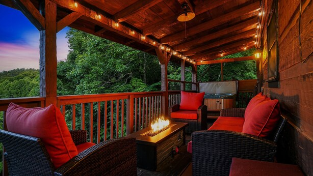 A covered outdoor seating area with wicker furniture, a fire feature, and string lights.
