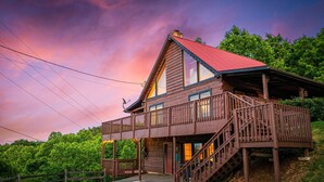 A wooden cabin with a red roof, a balcony, and a staircase leading to the entrance.