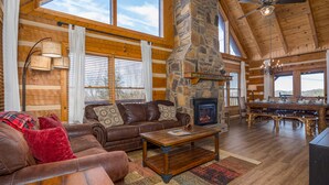 A cozy log cabin interior with a stone fireplace, wooden furniture, and large windows. - Mountain Views on 1 Acre ► 4 miles to Pigeon Forge ► Mini-Golf ► Dog Friendly (Sevierville)